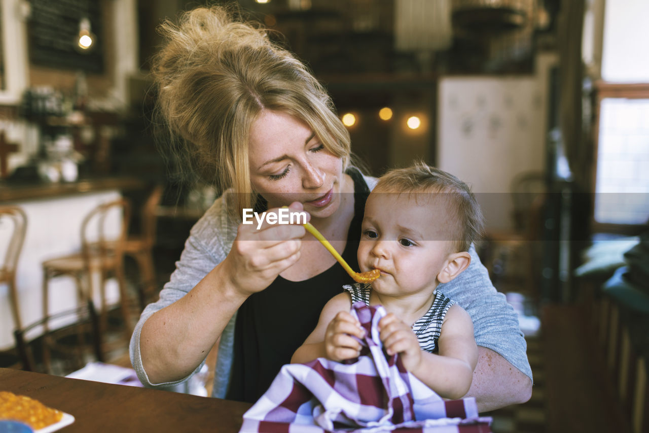 Mid adult mother feeding baby boy at restaurant table