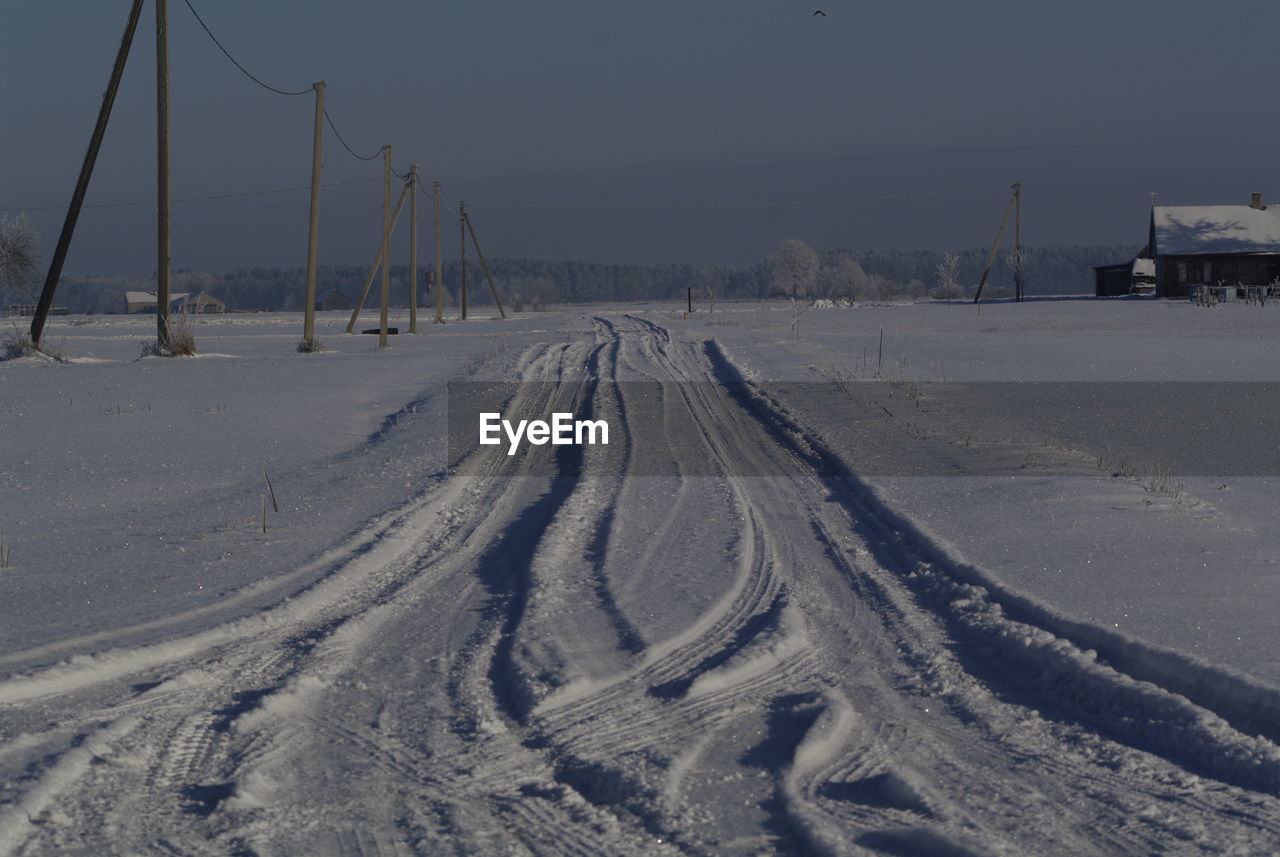 Tire tracks on snow field against sky