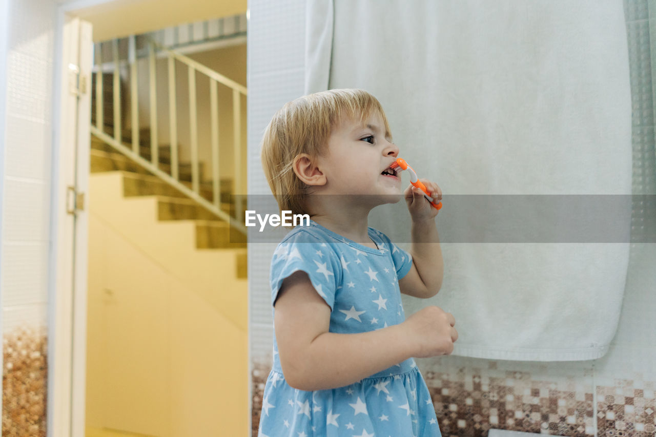 A little girl learns to brush her teeth on her own in the bathroom.