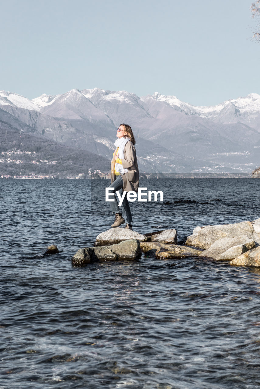 Woman standing on rock by sea against clear sky