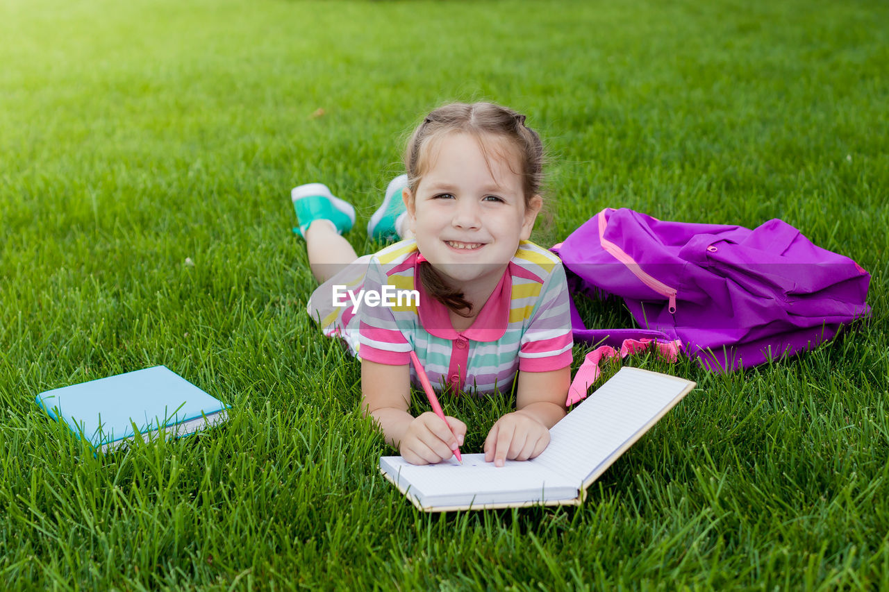 Portrait of smiling girl writing in book while lying on grassy land