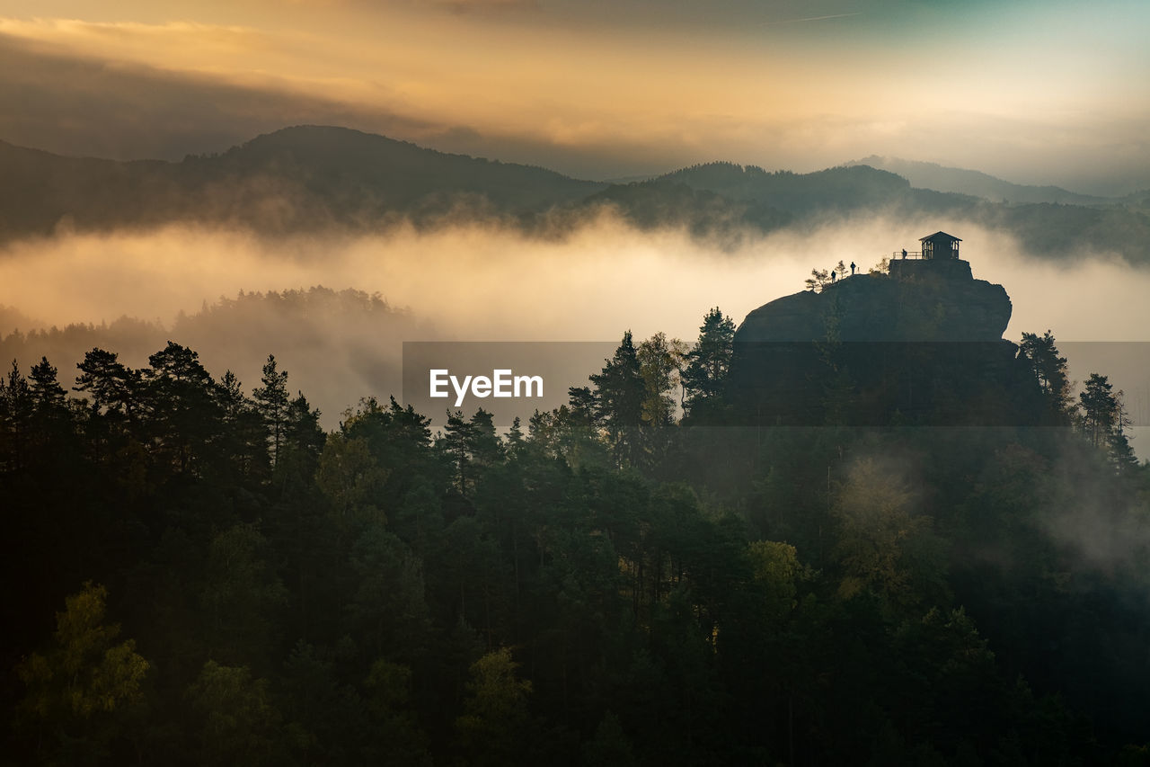 Islands above misty valley, mountain peak with cabin at sunrise. autumn weather with orange mist