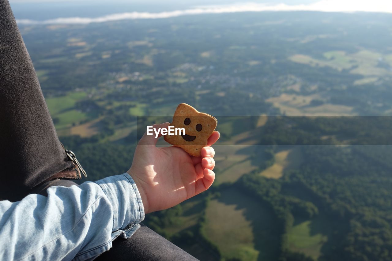 Cropped image of person holding biscuit in hot air balloon over landscape