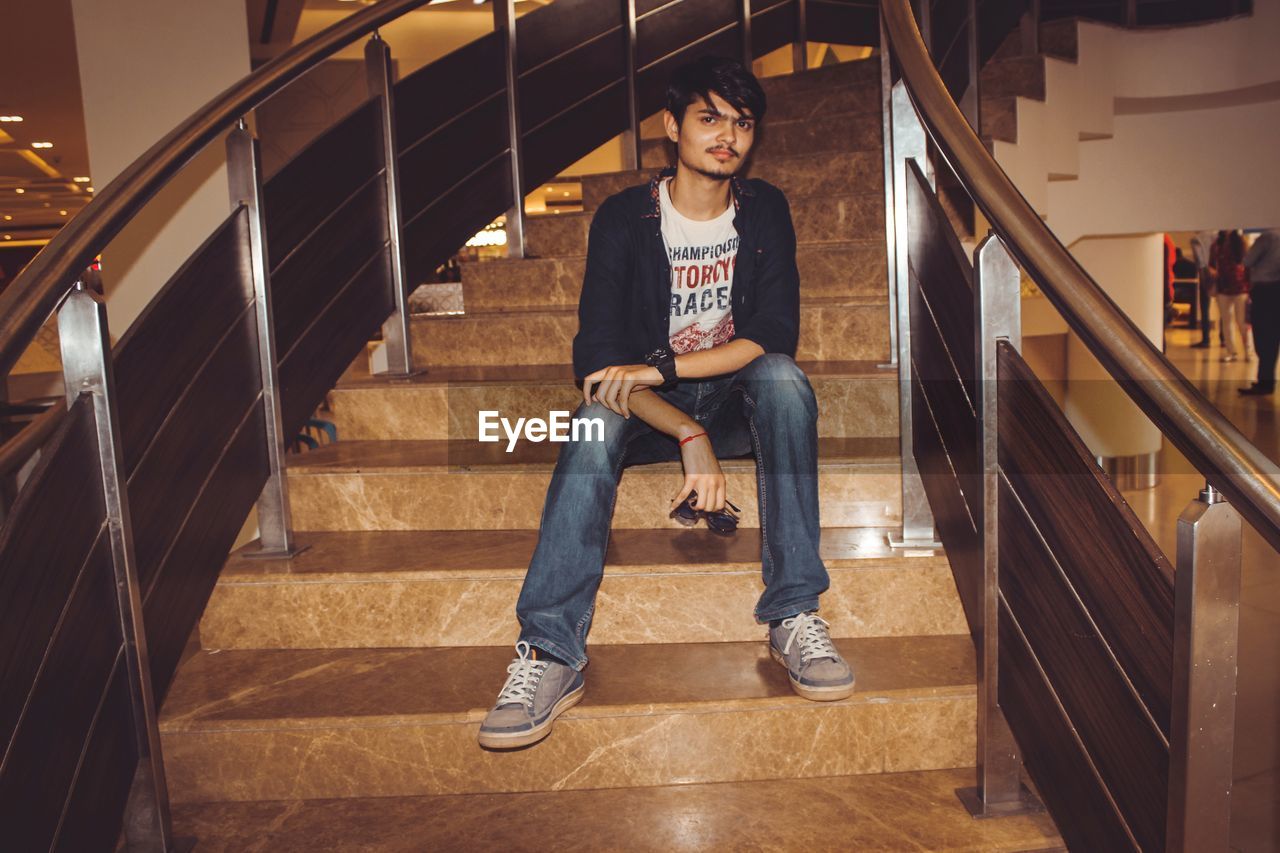 PORTRAIT OF A YOUNG MAN SITTING ON STAIRCASE