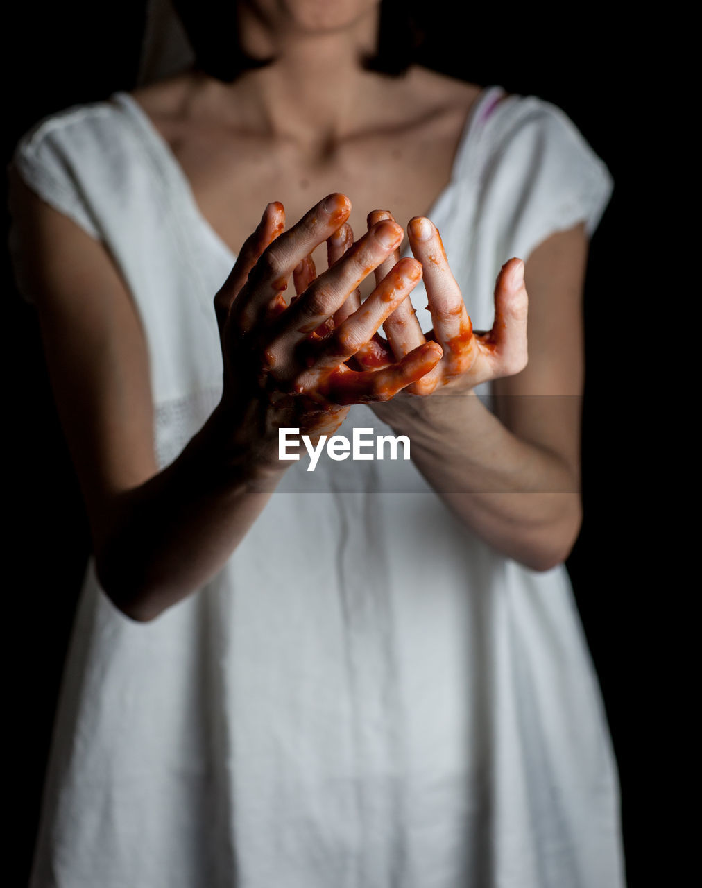 Midsection of woman with blood hands against black background