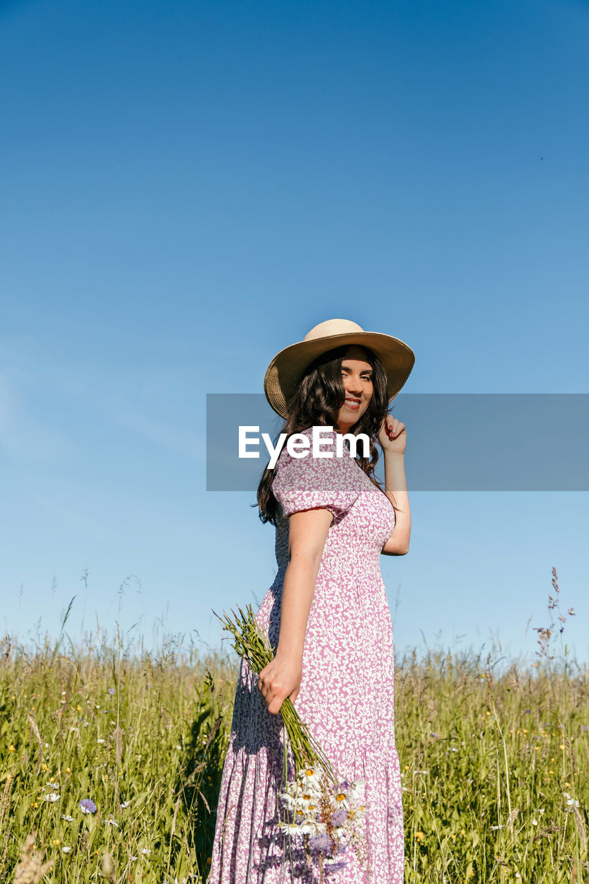 Beautiful woman standing in field, holding wildflowers