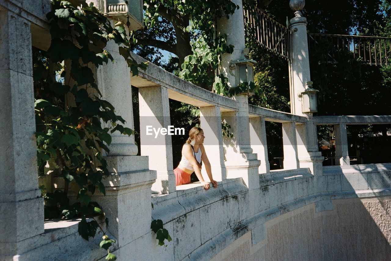 WOMAN SITTING BY BUILDING AGAINST TREES