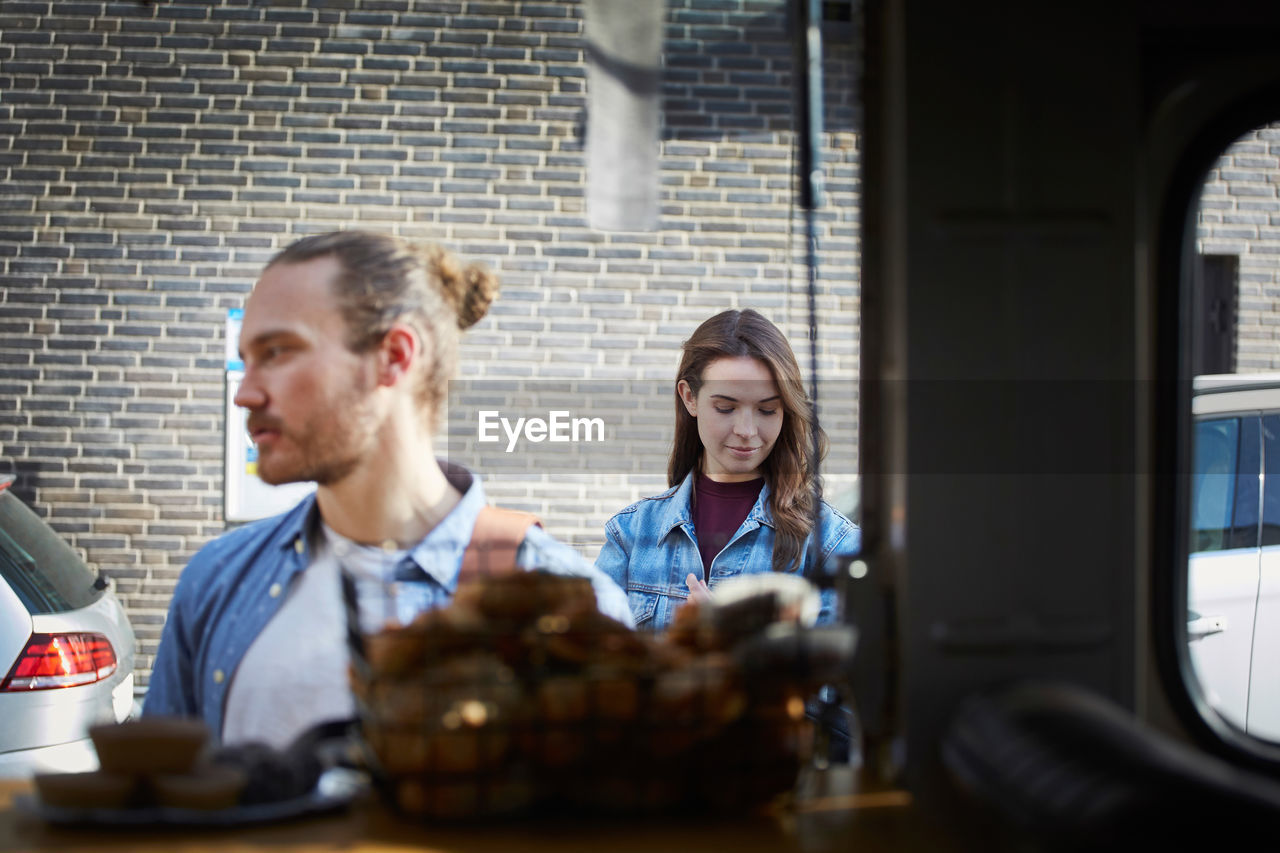 Young man and woman standing at food truck in city