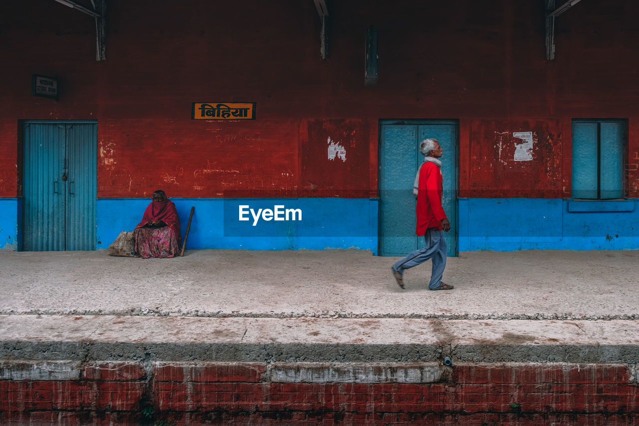 FULL LENGTH REAR VIEW OF MAN WALKING ON FOOTPATH AGAINST WALL