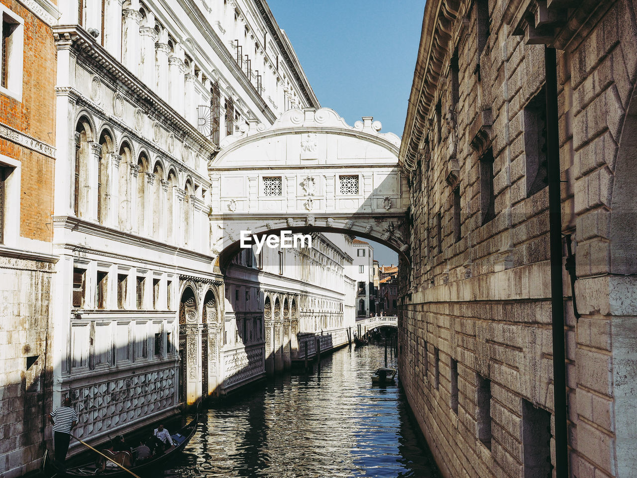 Canal amidst buildings against blue sky in city during sunny day