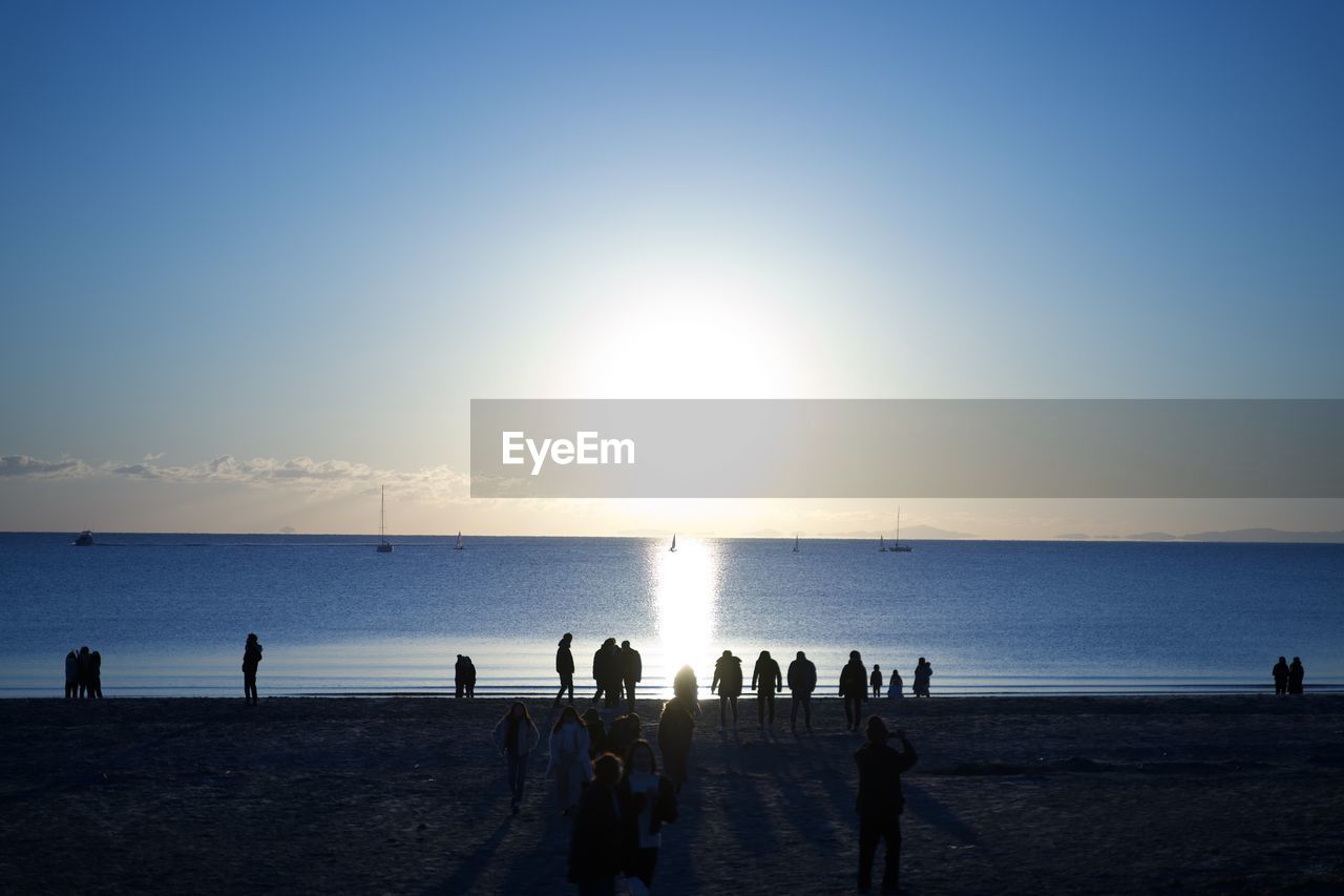 Silhouette people on beach against sky during sunset