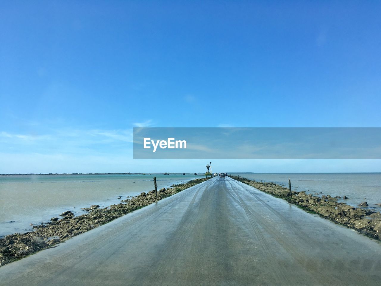 Empty road along calm sea against sky