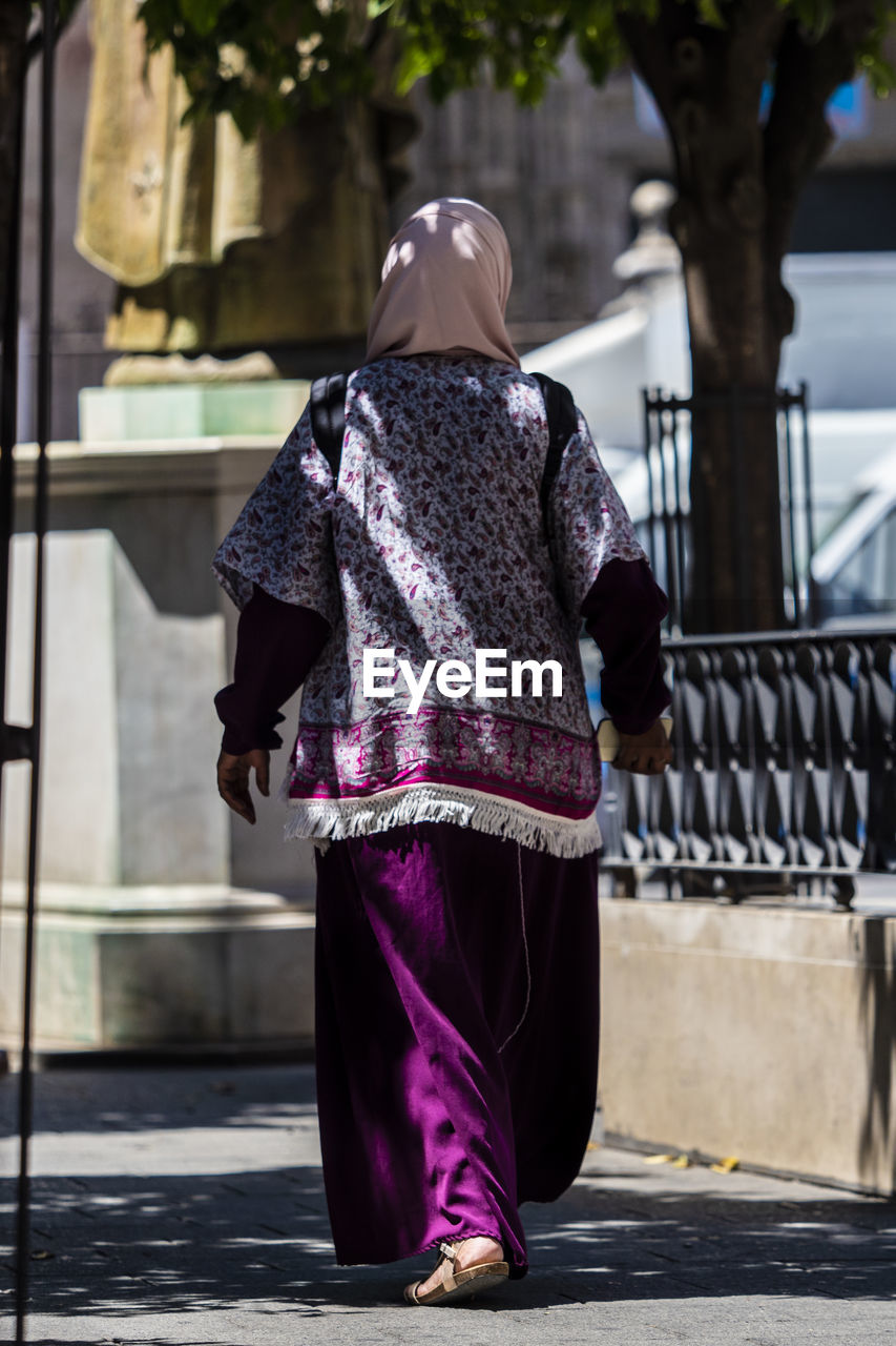 REAR VIEW OF A WOMAN WALKING ON FOOTPATH