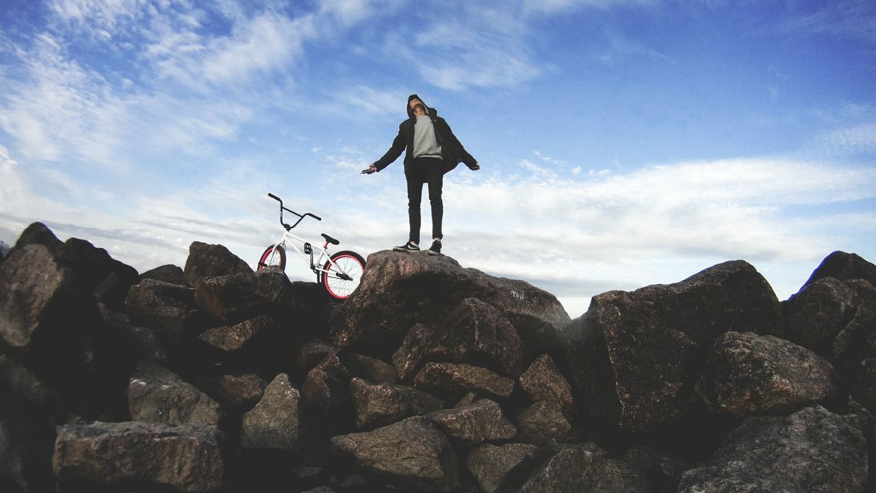 Low angle view of man standing on rock against sky