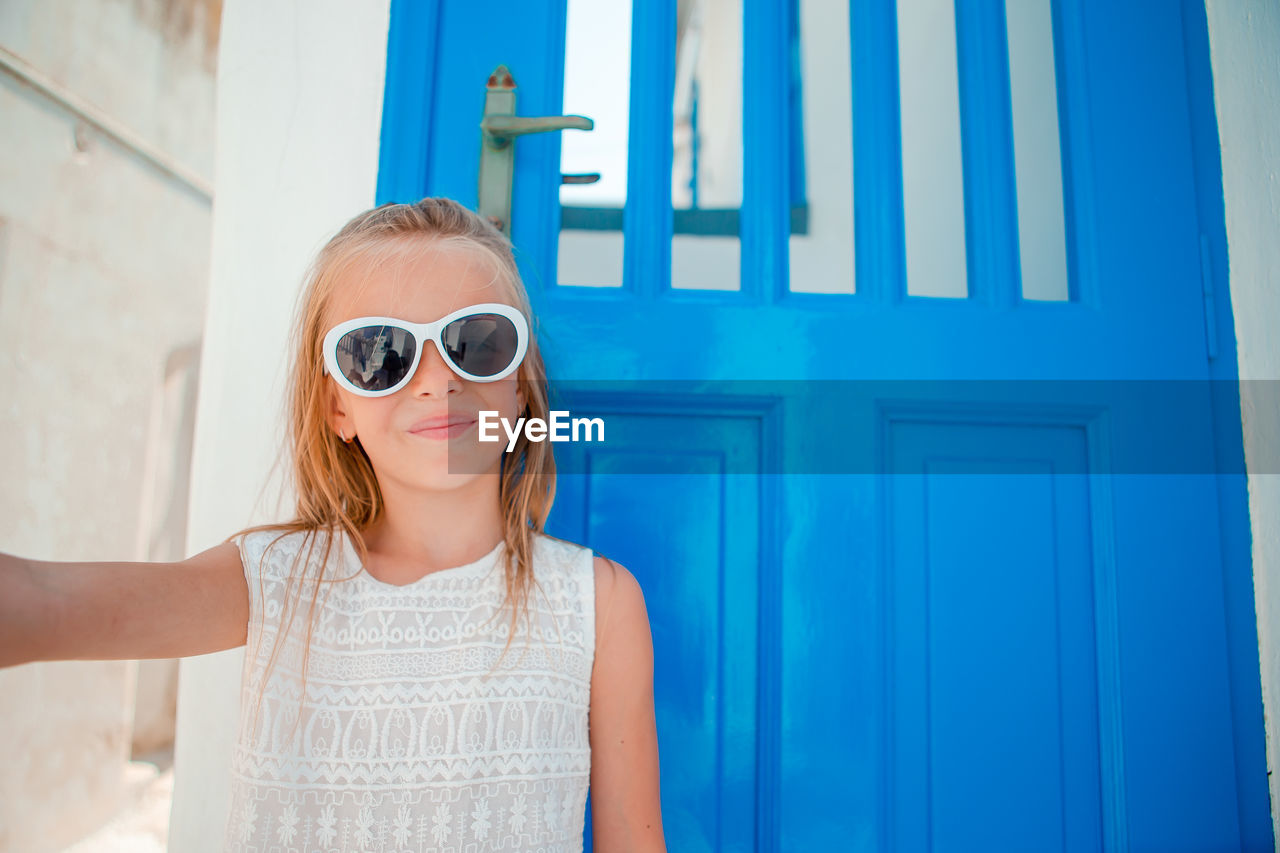 portrait of young woman wearing sunglasses while standing against wall