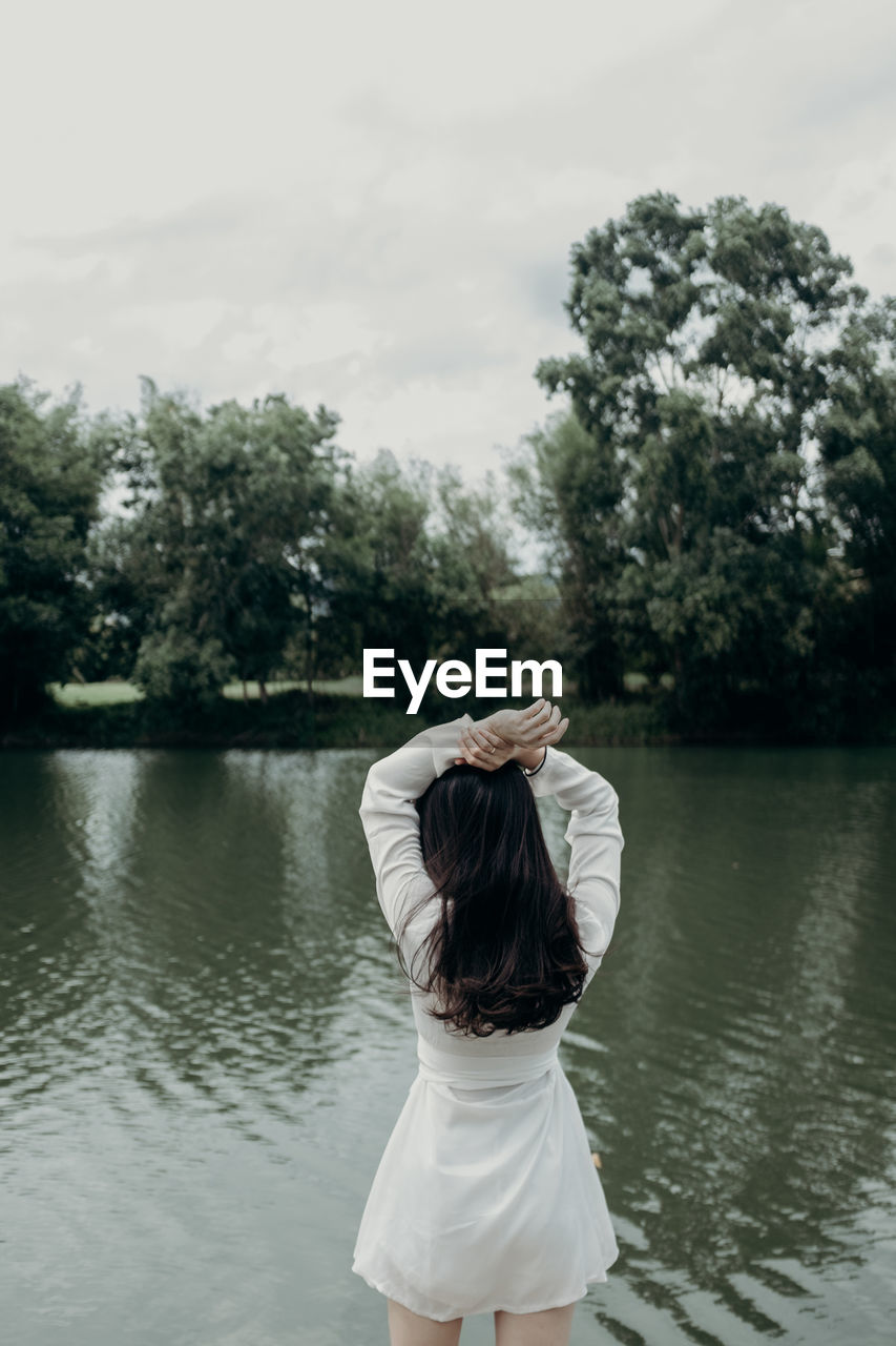 Rear view of woman standing at lakeshore against sky