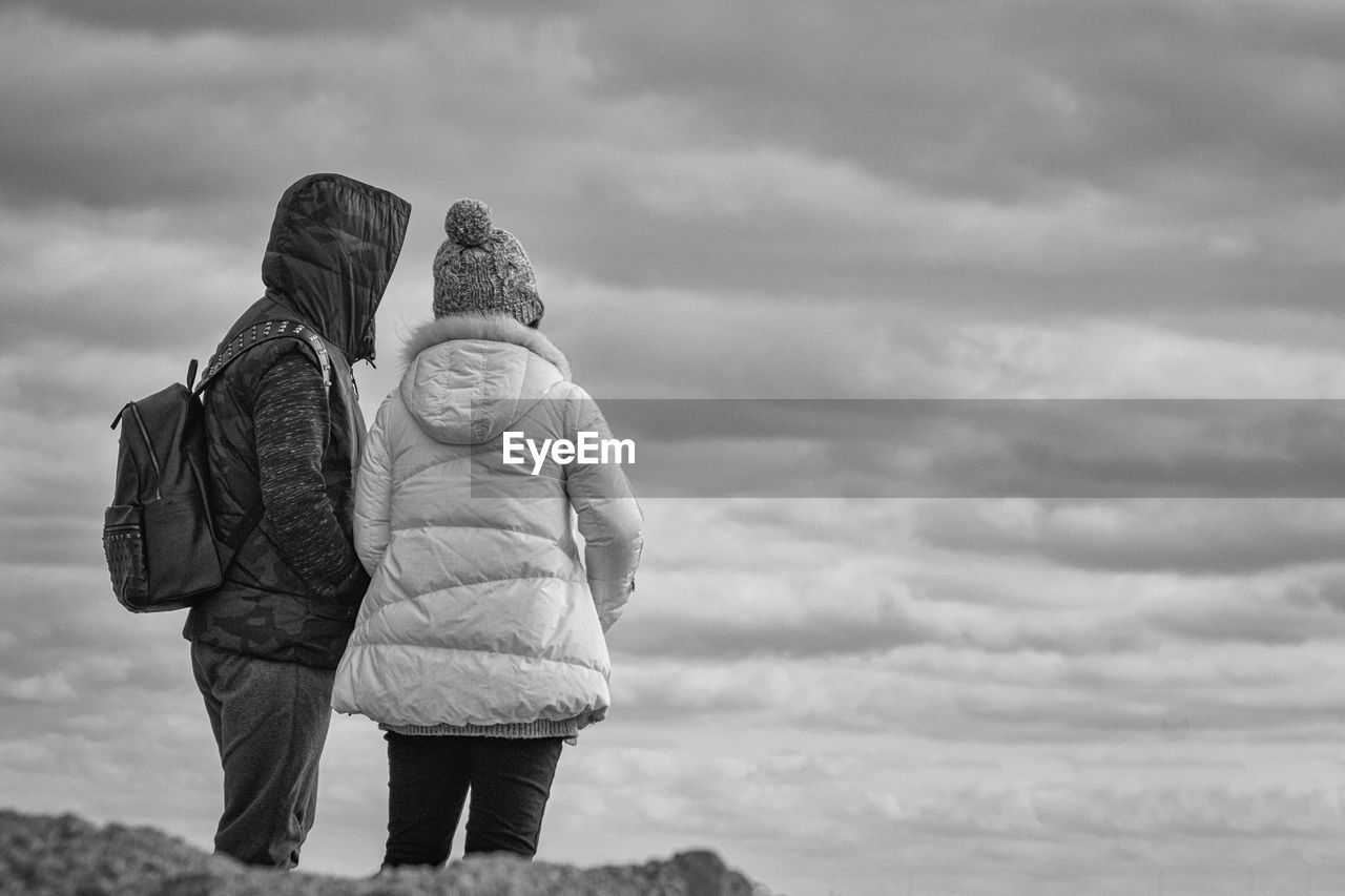 Rear view of couple standing against cloudy sky