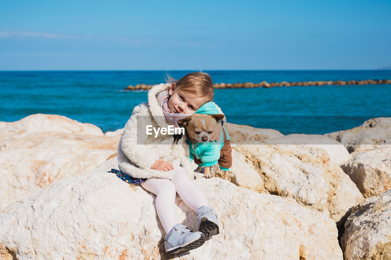 Portrait of cute girl with dog sitting on rock