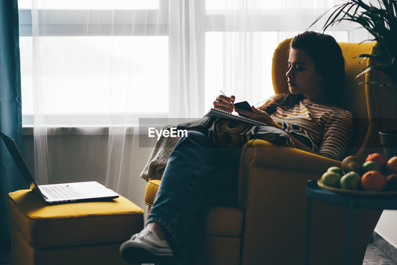 young woman using digital tablet while sitting on sofa at home