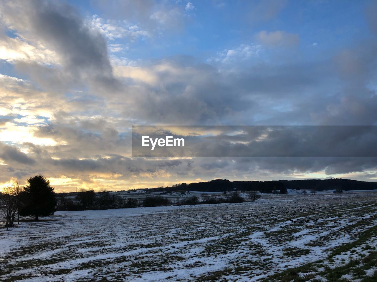 SCENIC VIEW OF SNOW COVERED FIELD AGAINST SKY AT SUNSET