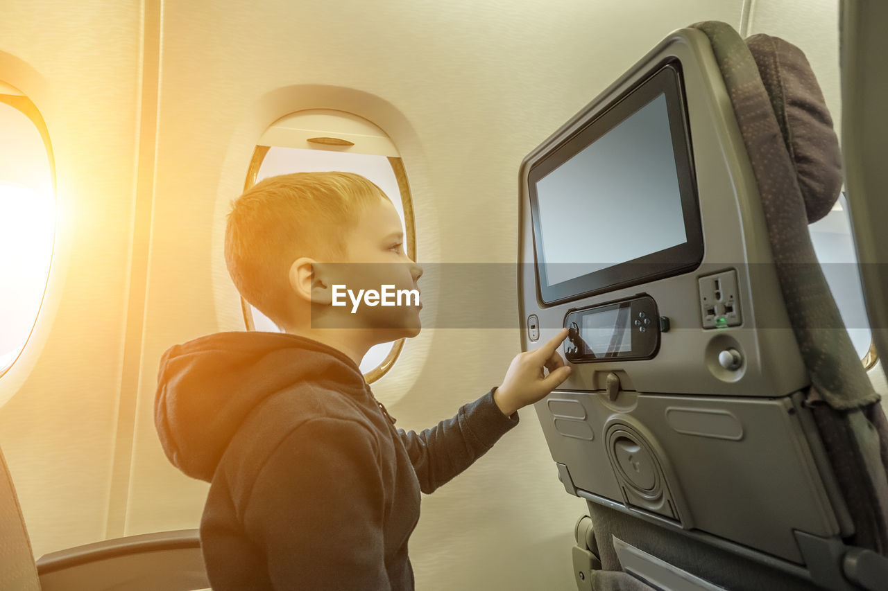 Little boy traveling by airplane. child sitting by aircraft window and looking on monitor. traveling