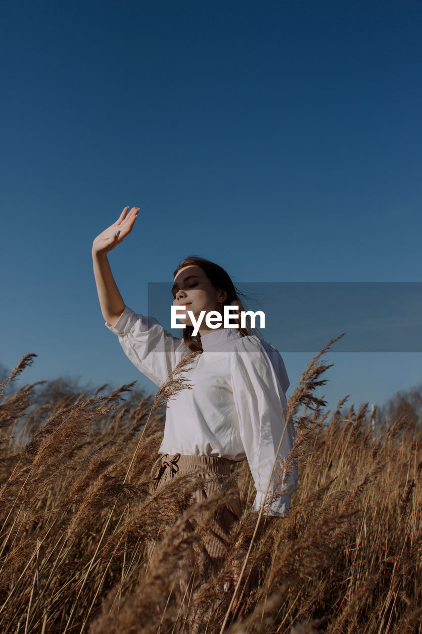 Young woman standing on field against clear blue sky