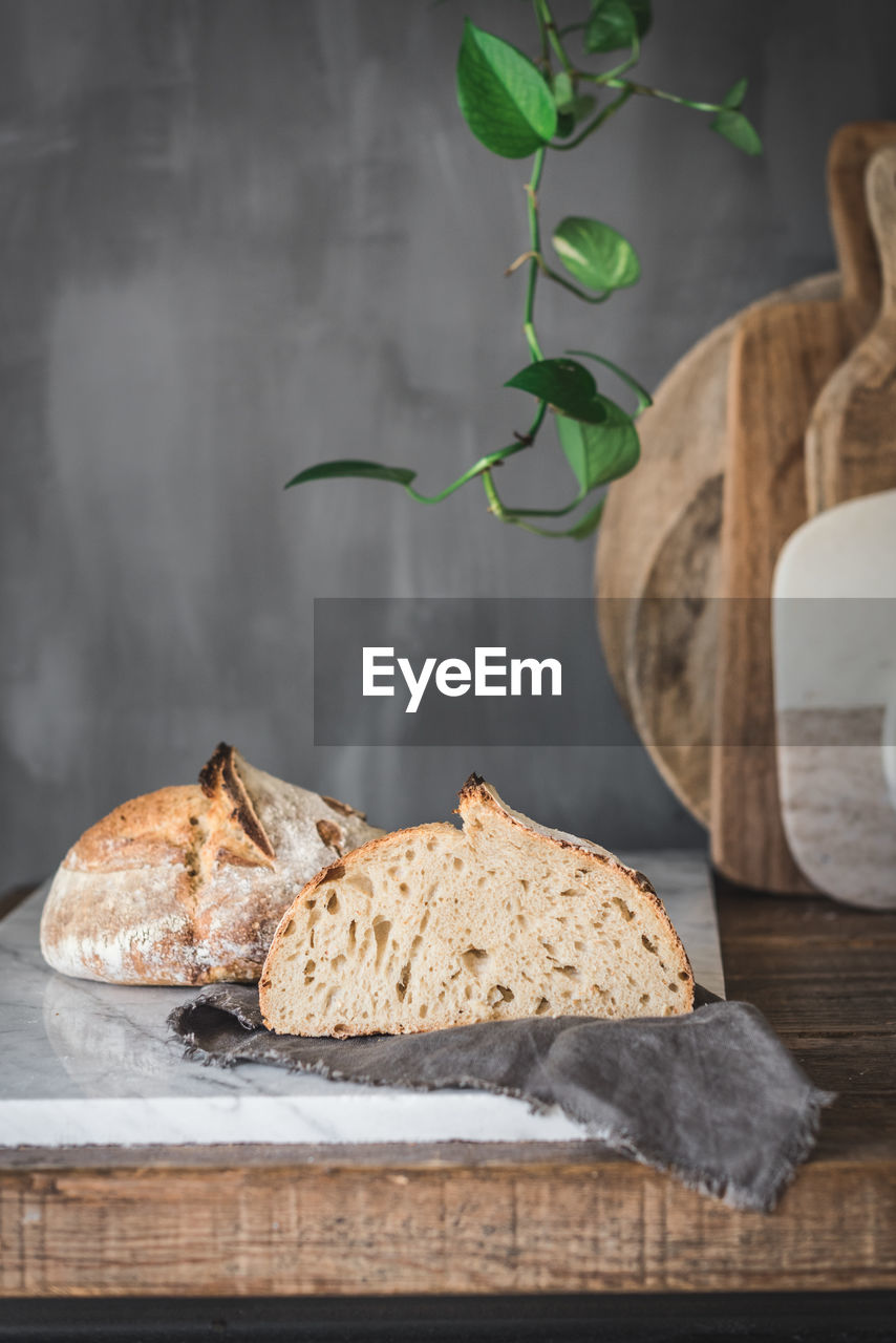 Cut loaf of fresh baked bread with crispy crust placed on marble tabletop in stylish kitchen