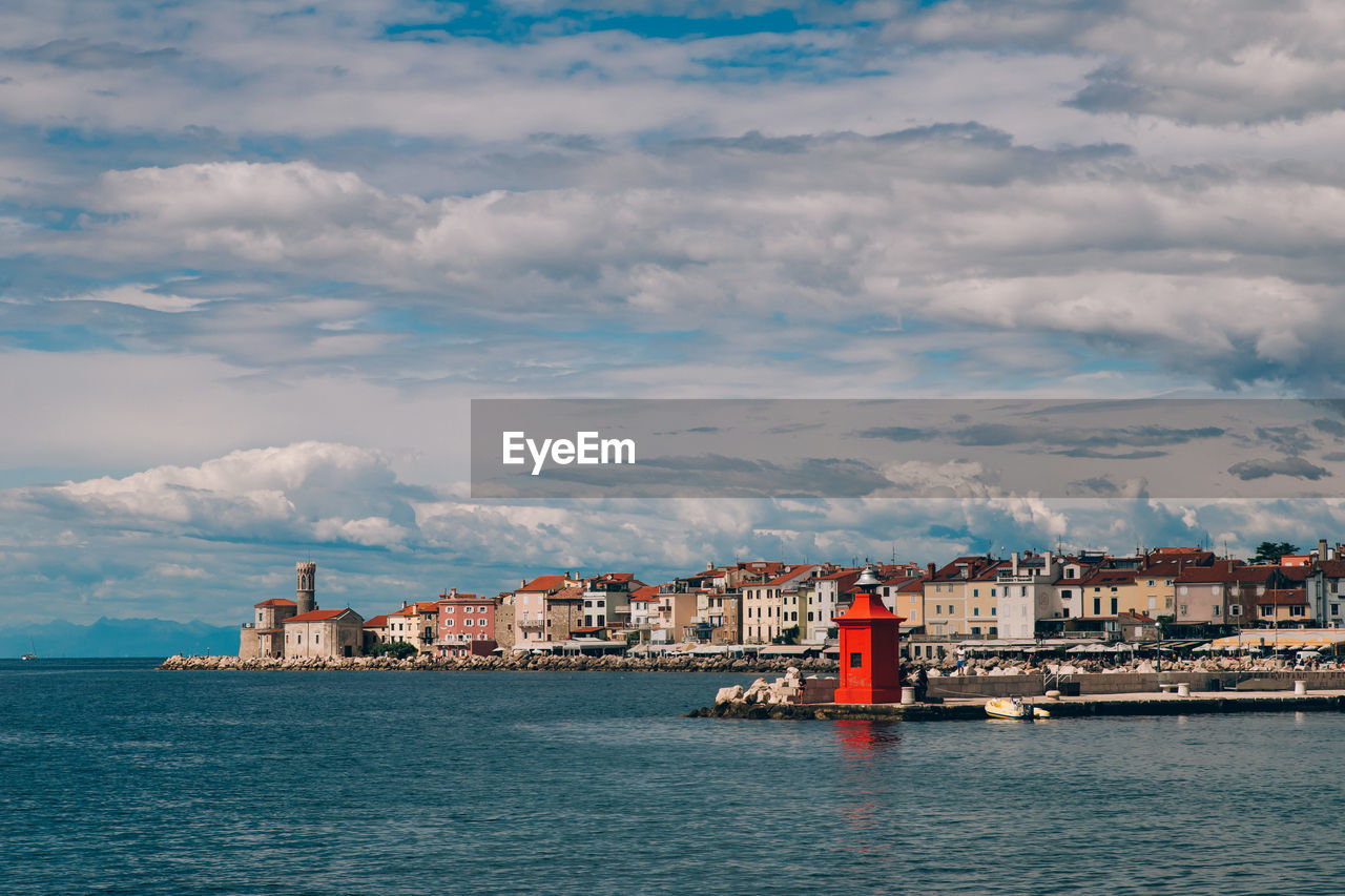 Buildings at waterfront against cloudy sky