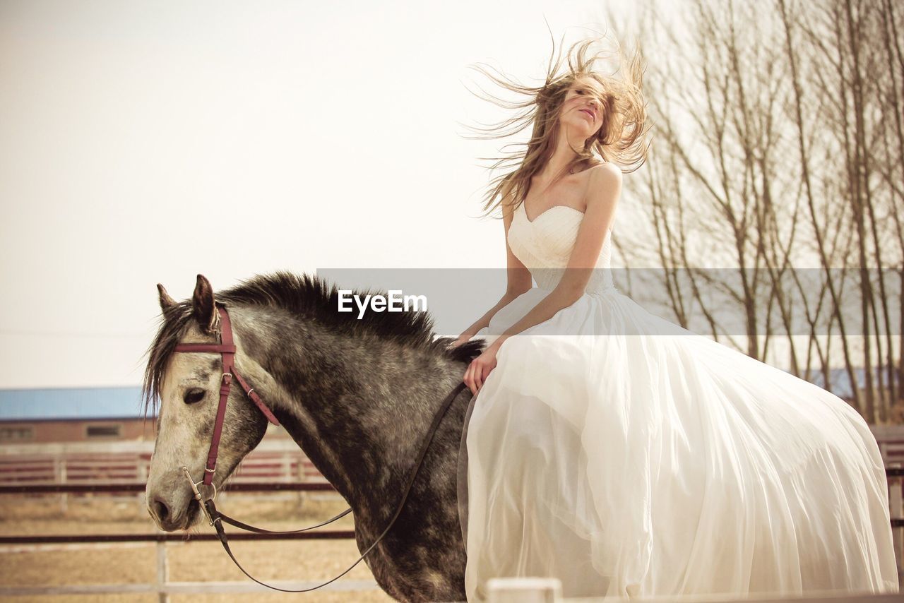 Beautiful bride riding horse on field against sky