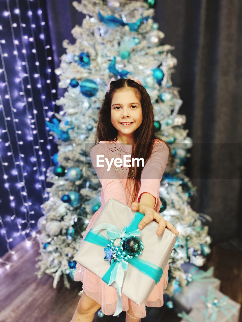 Portrait of smiling girl holding gift box sitting against christmas tree