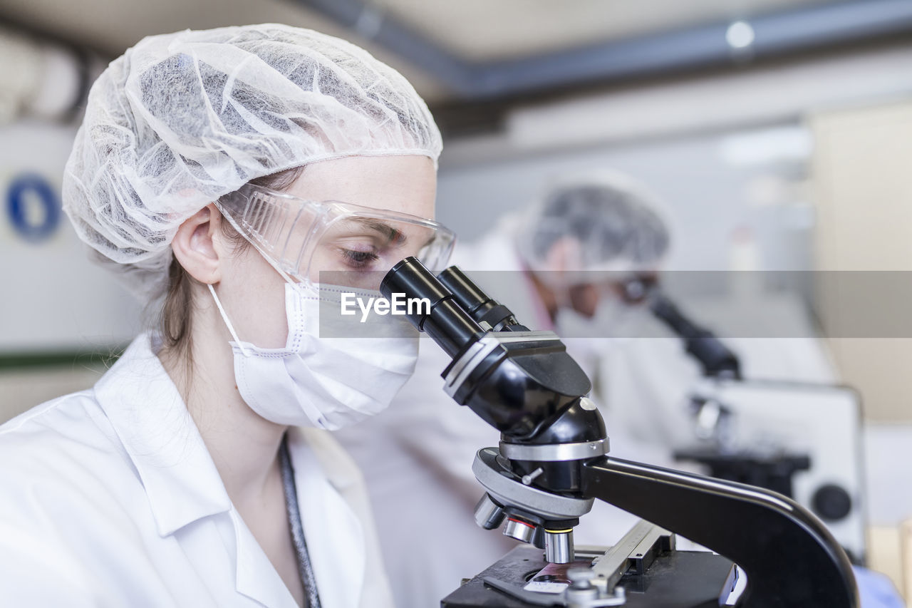 Woman and man scientists looking through microscope at laboratory