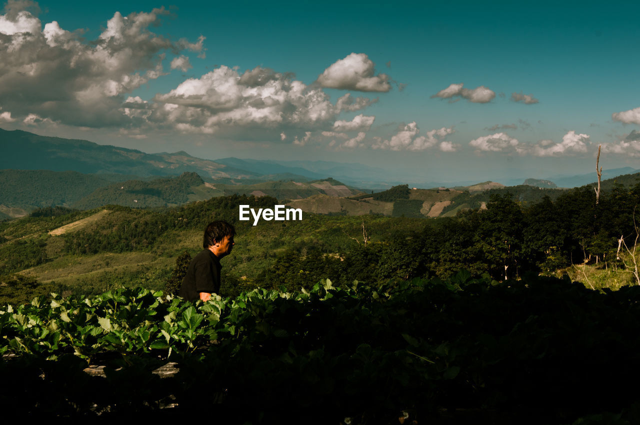 MAN STANDING BY PLANTS AGAINST SKY