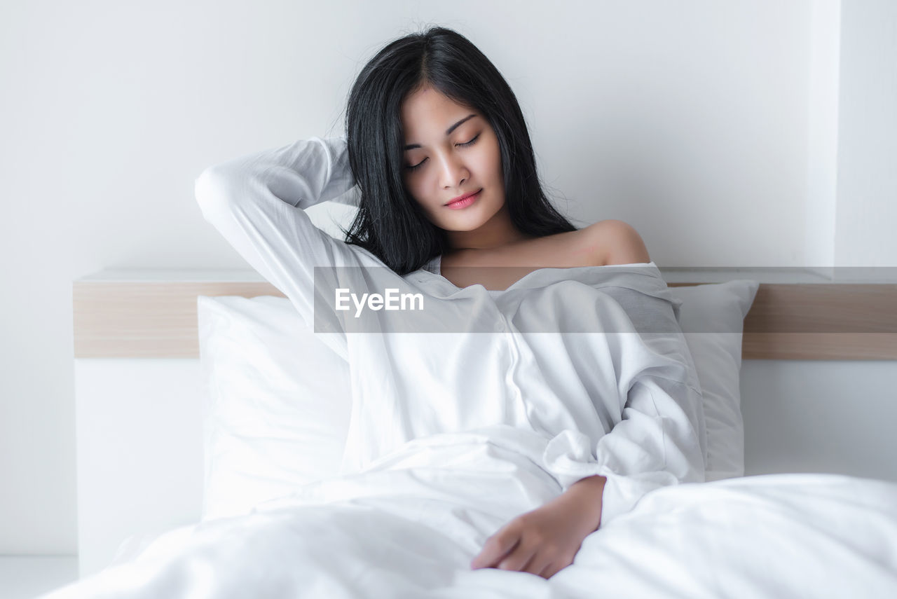 Young woman waking up while sitting on bed at home