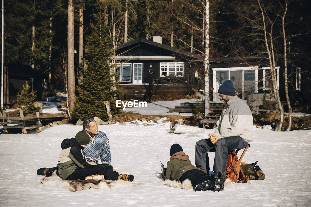 Smiling mature men with boys ice fishing on snow during sunny day