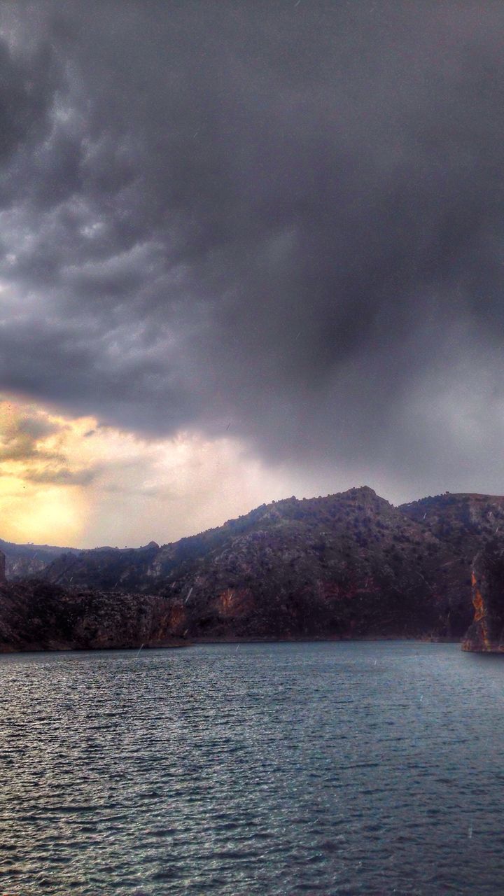 Scenic view of lake by mountain against cloudy sky