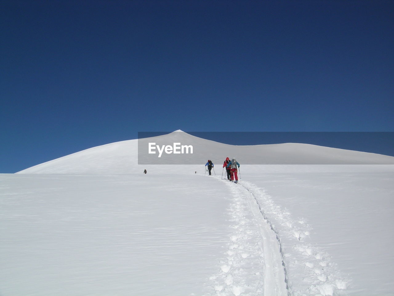 Rear view of people walking on snowcapped mountain against clear sky