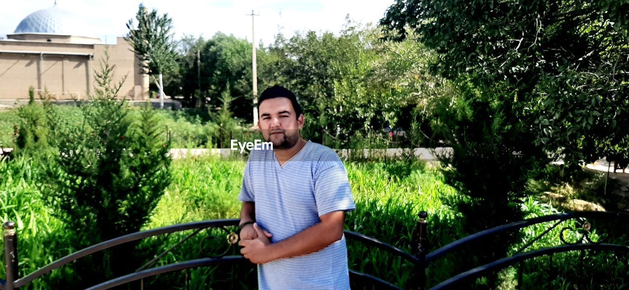 YOUNG MAN STANDING AGAINST TREES AND PLANTS