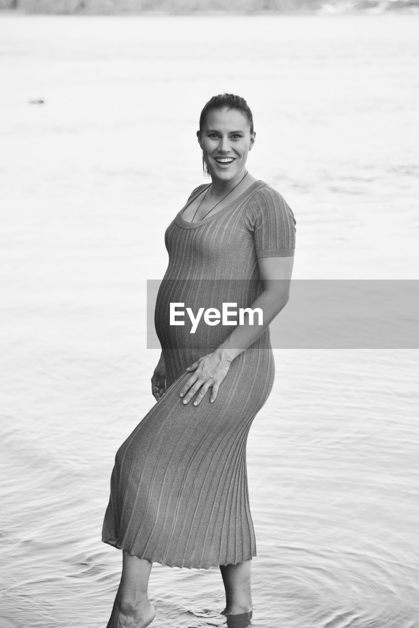 Portrait of smiling pregnant woman standing by sea 