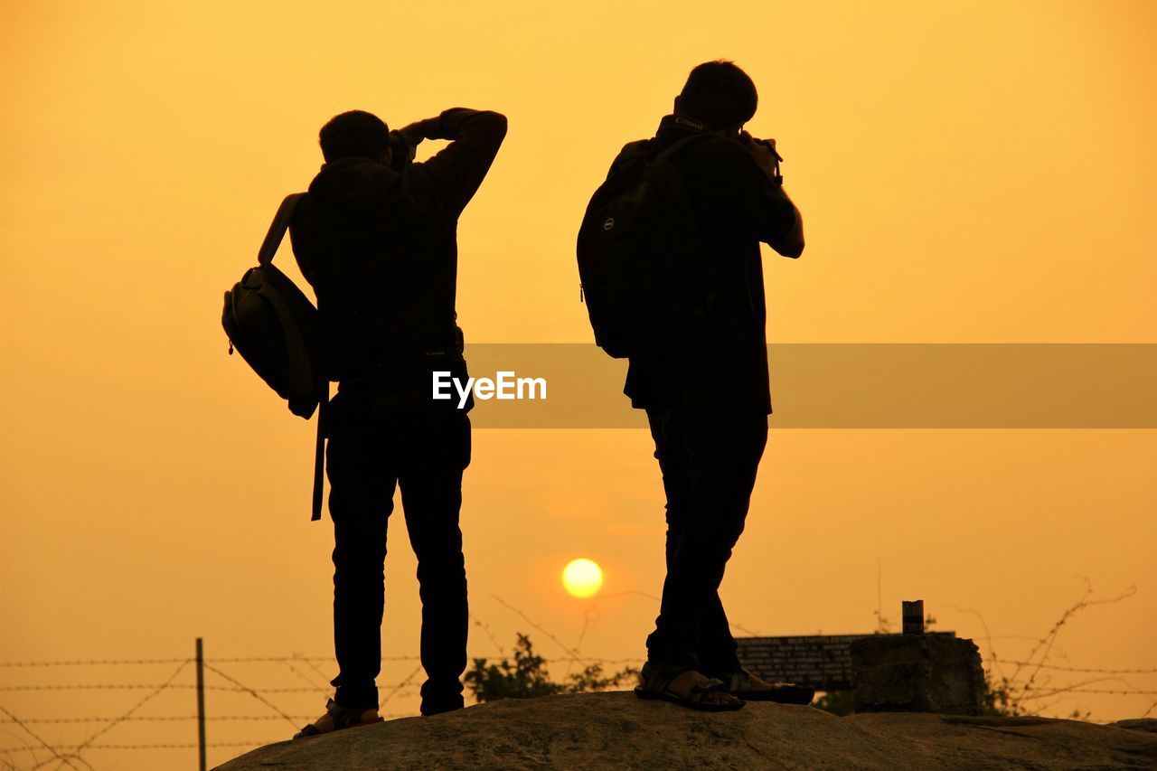 Silhouette men standing against orange sky