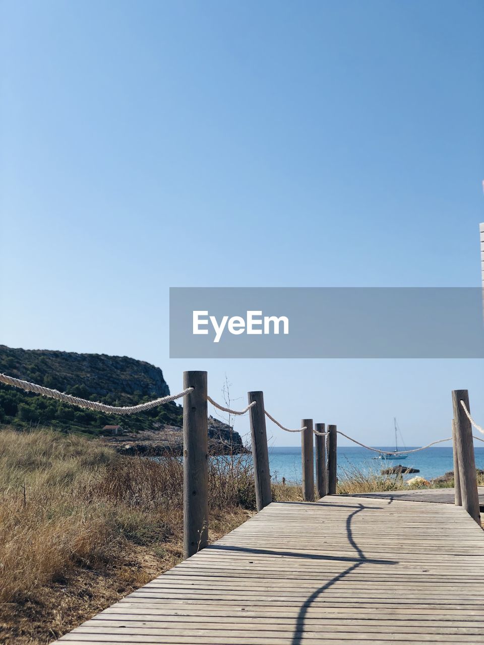 Wooden walkway leading towards sea against clear blue sky