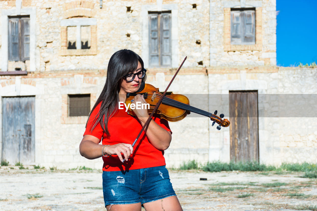 Woman playing violin while standing against building