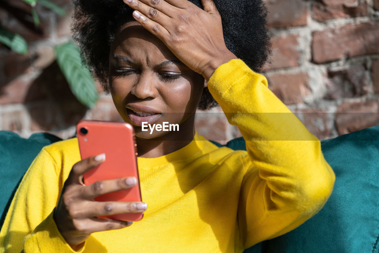 Thoughtful woman using smart phone while sitting home