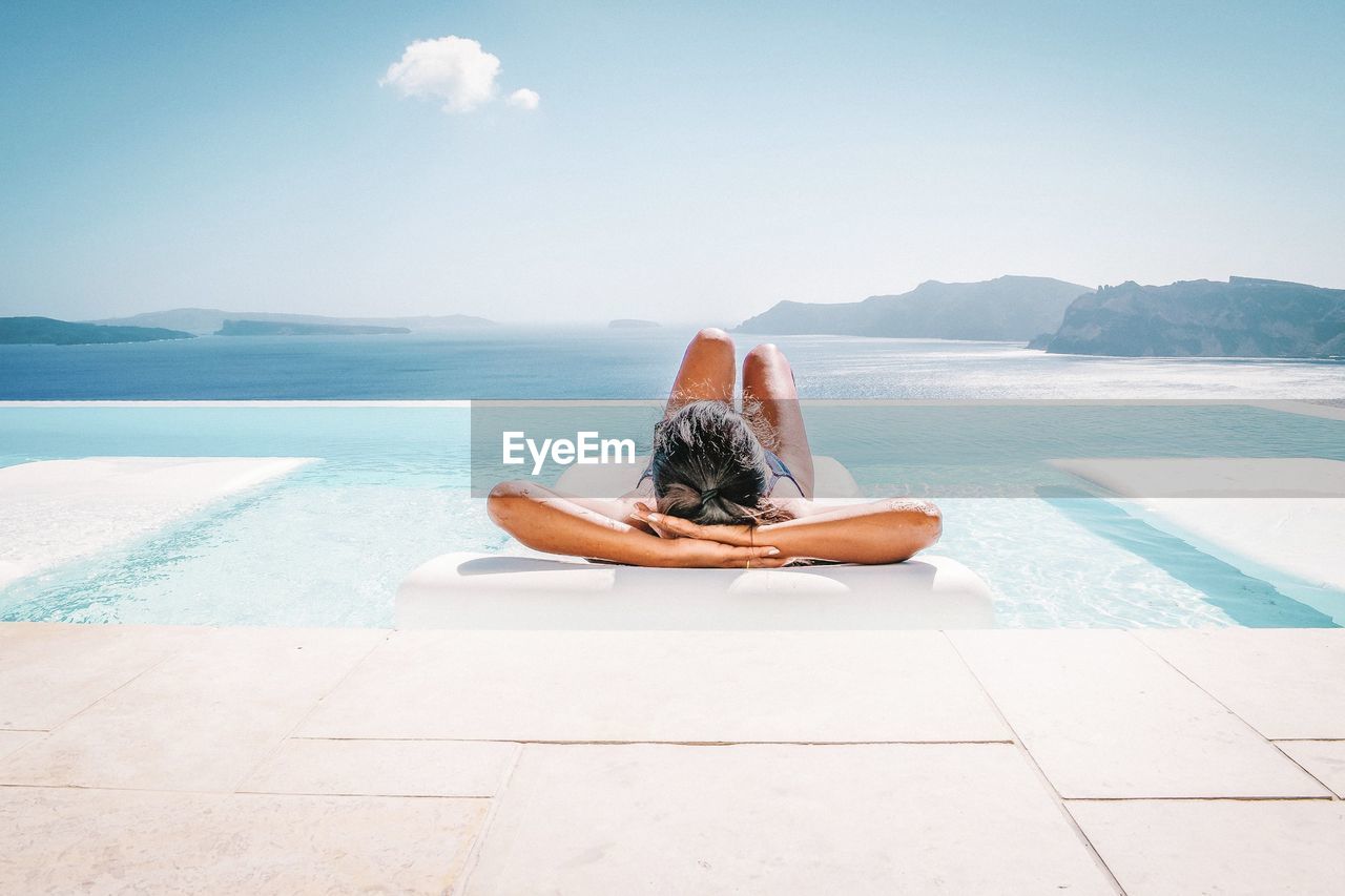 Woman relaxing on pool raft floating on swimming pool against sky