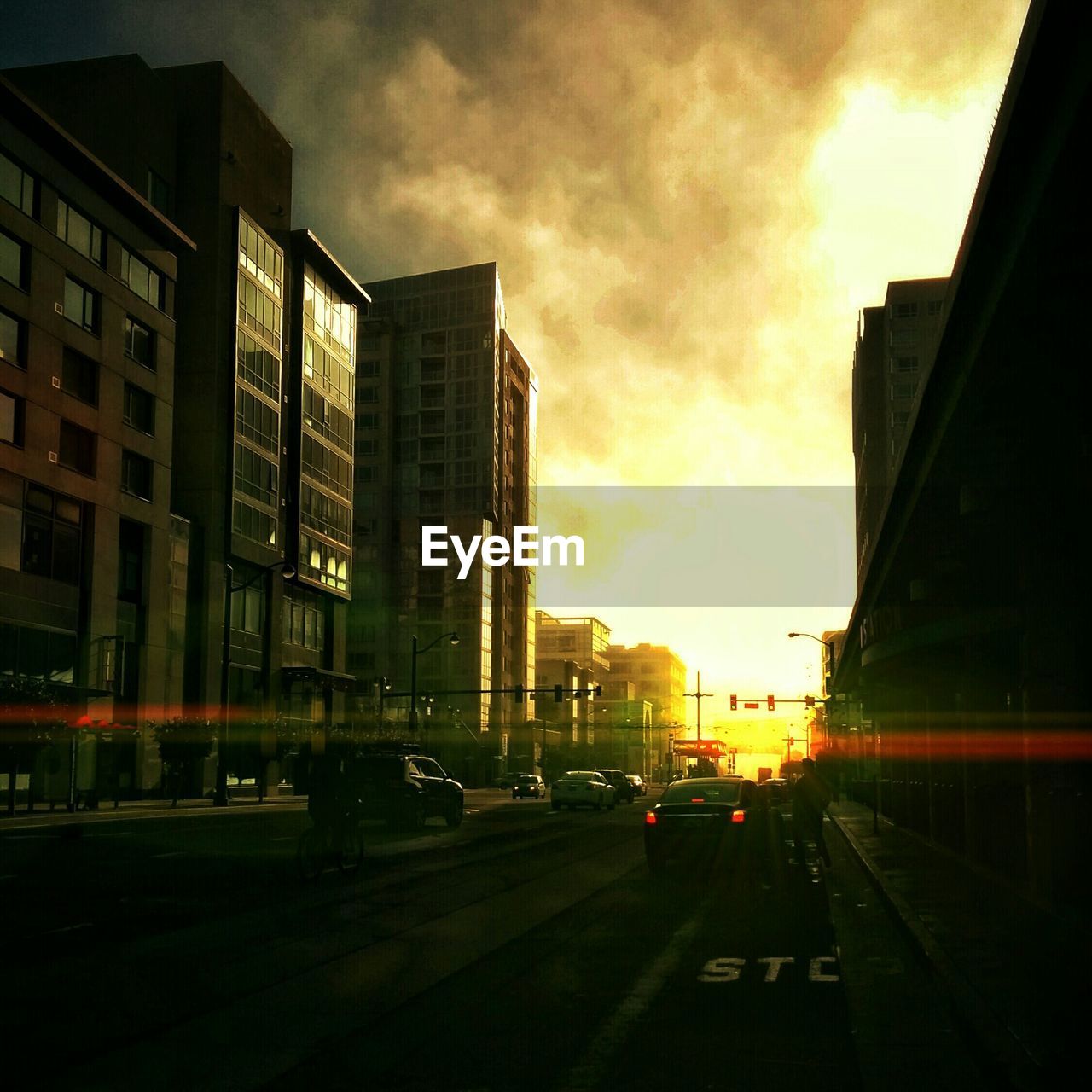 Cars on street amidst buildings against cloudy sky during sunset