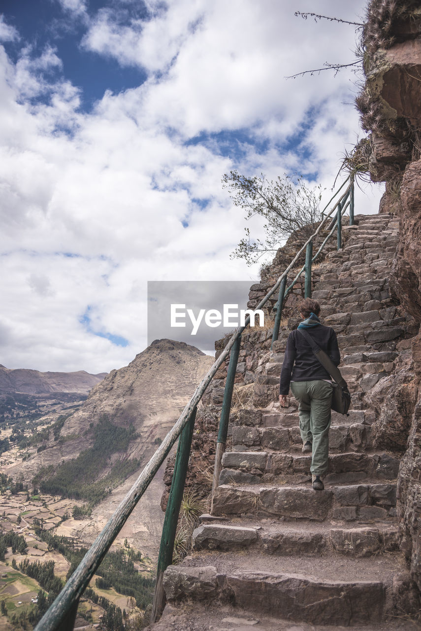 Rear view full length of man moving up on steps against cloudy sky