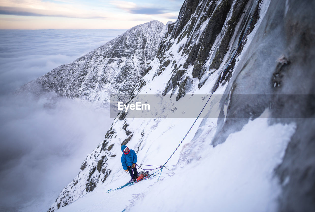 A male climber belaying his lead during a cold winter alpine climb