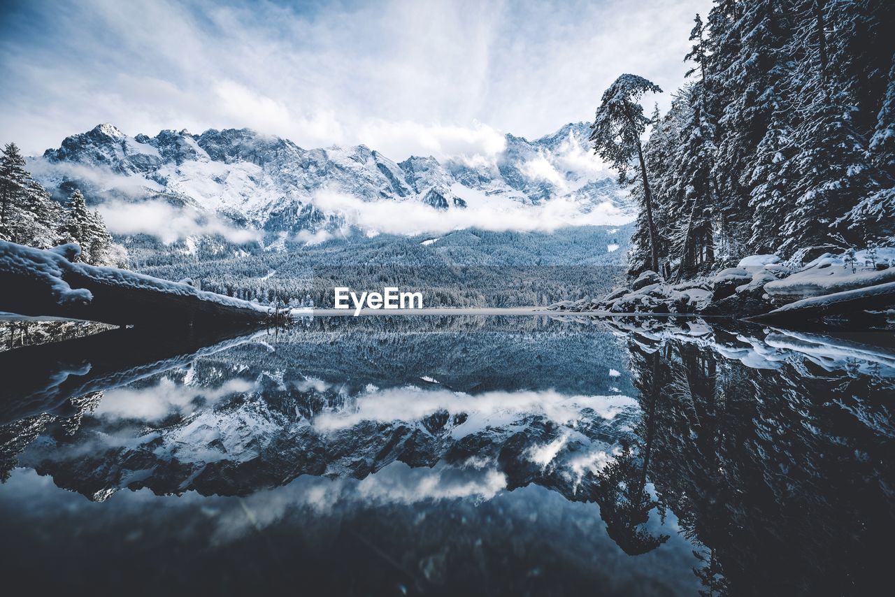 Scenic view of calm lake by snow covered mountains against sky