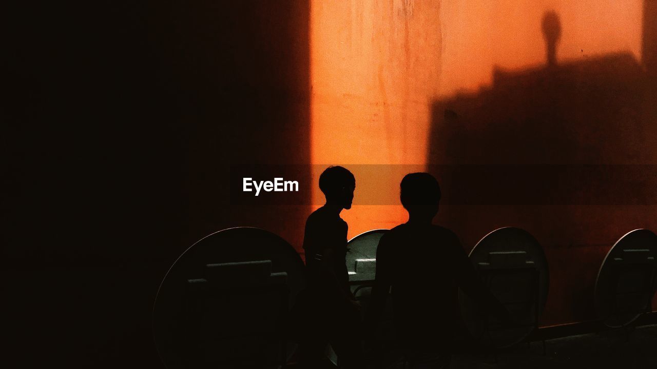 Silhouette men standing against orange wall