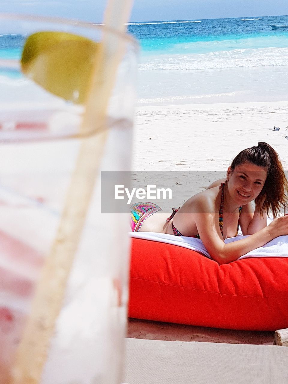 Close-up of drink with woman lying in background at beach