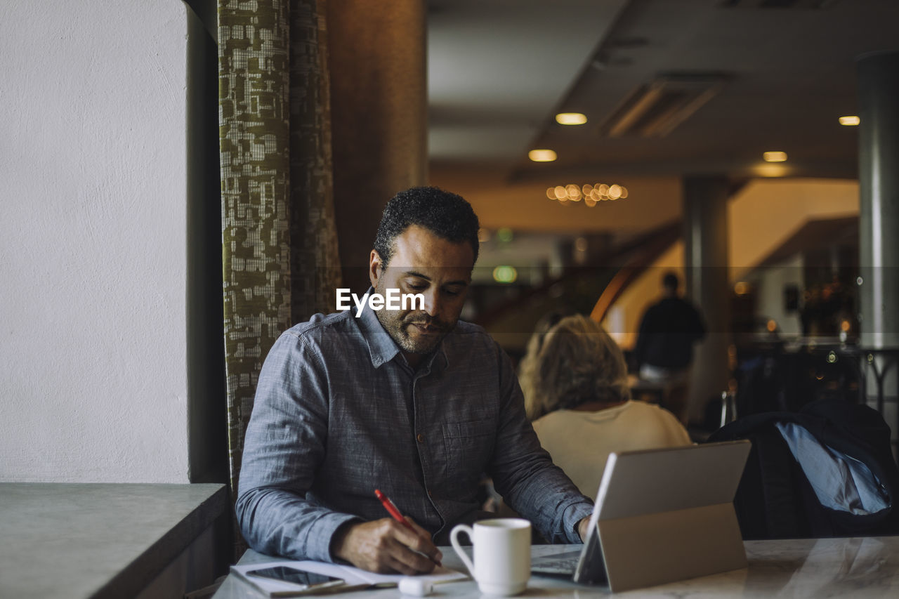 Male freelancer writing in diary while sitting with laptop at table